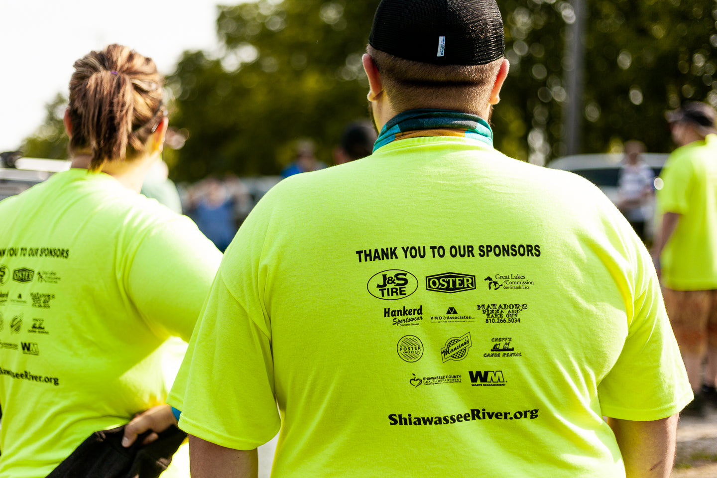 Person wearing a bright yellow t-shirt with sponsor logos and text, standing outdoors.